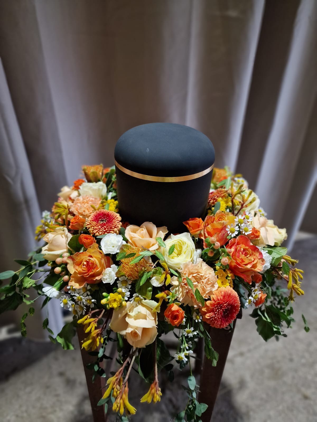 Schwarze Urne mit umlaufendem Blumenkranz aus Rosen und Chrysanthemen in Orange und Apricot