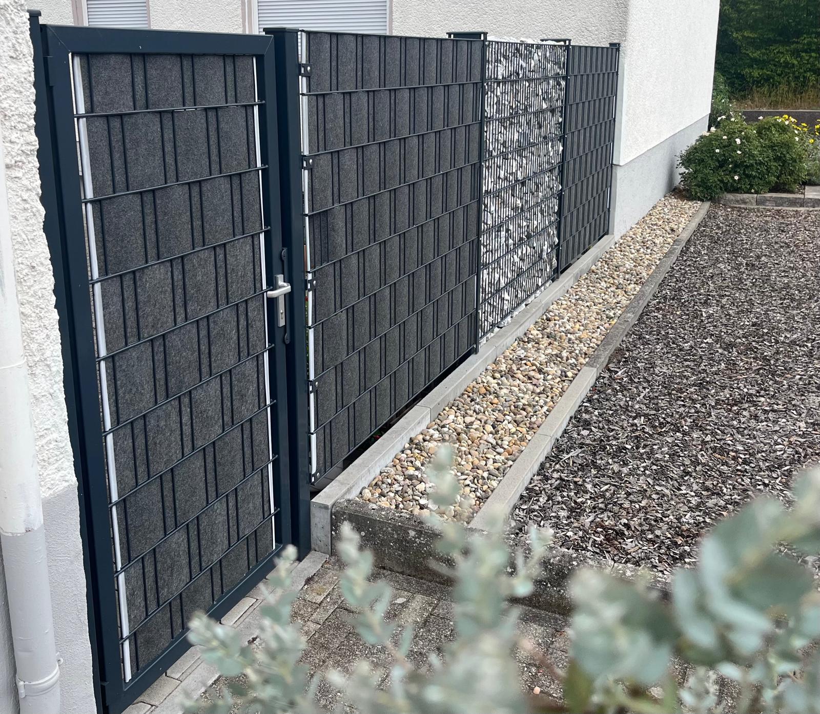 Anthrazitfarbenes Gartentor mit Sichtschutzstreifen neben einer Kiesfläche