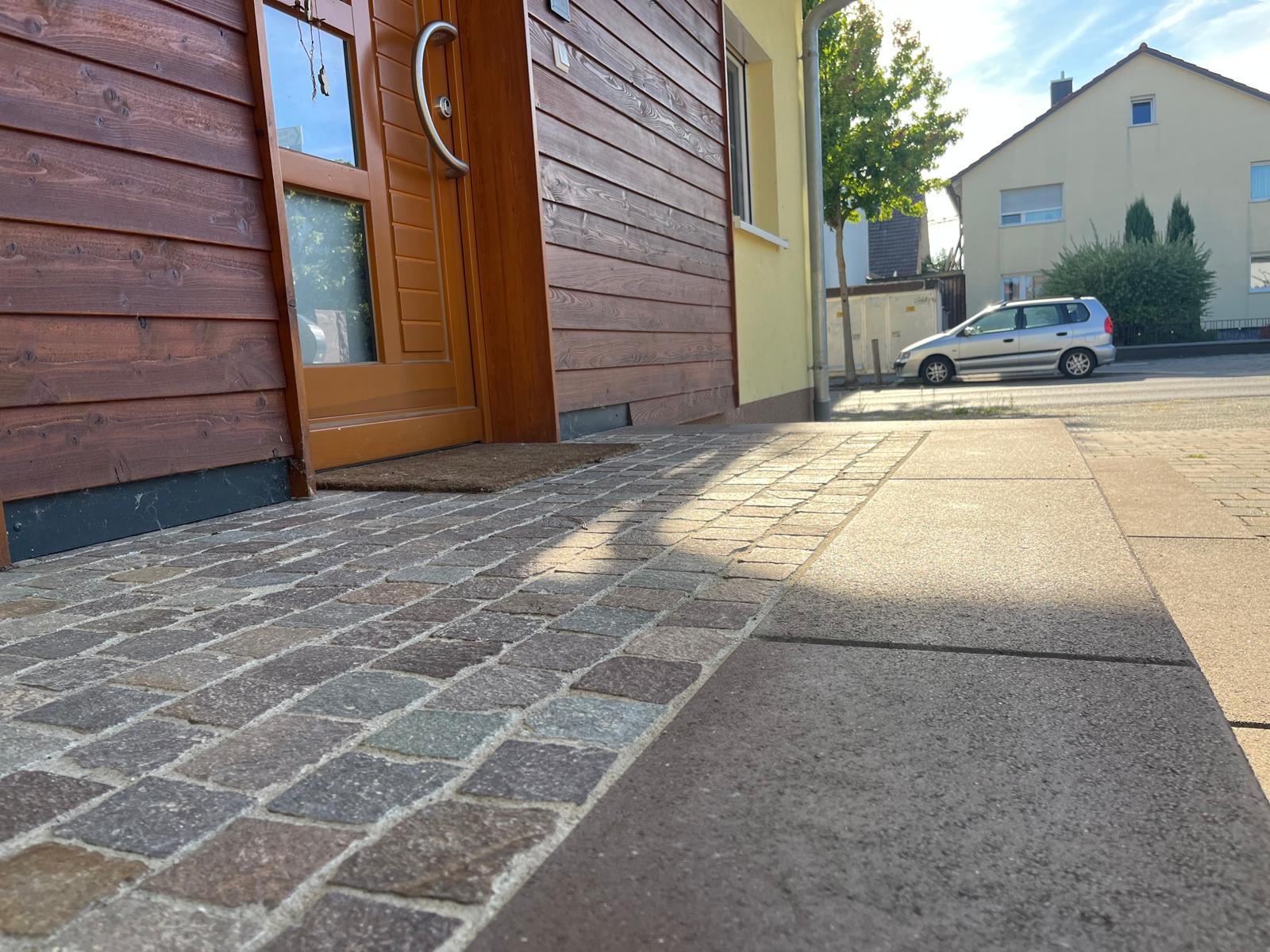 Neu verlegtes Natursteinpflaster vor einem Hauseingang mit Holzfassade