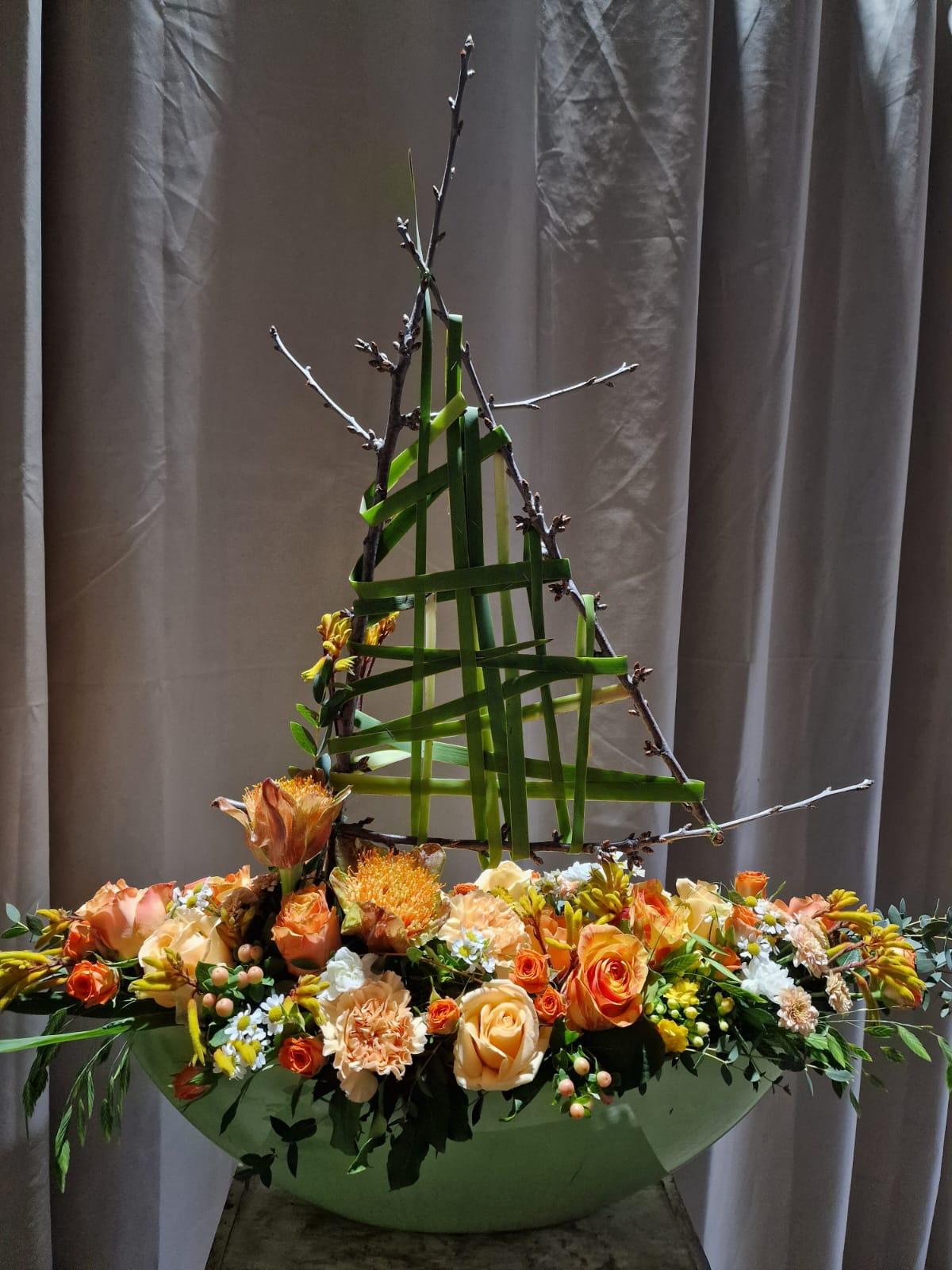 Längliches Blumengesteck in Orange- und Gelbtönen in einer hellen Schale